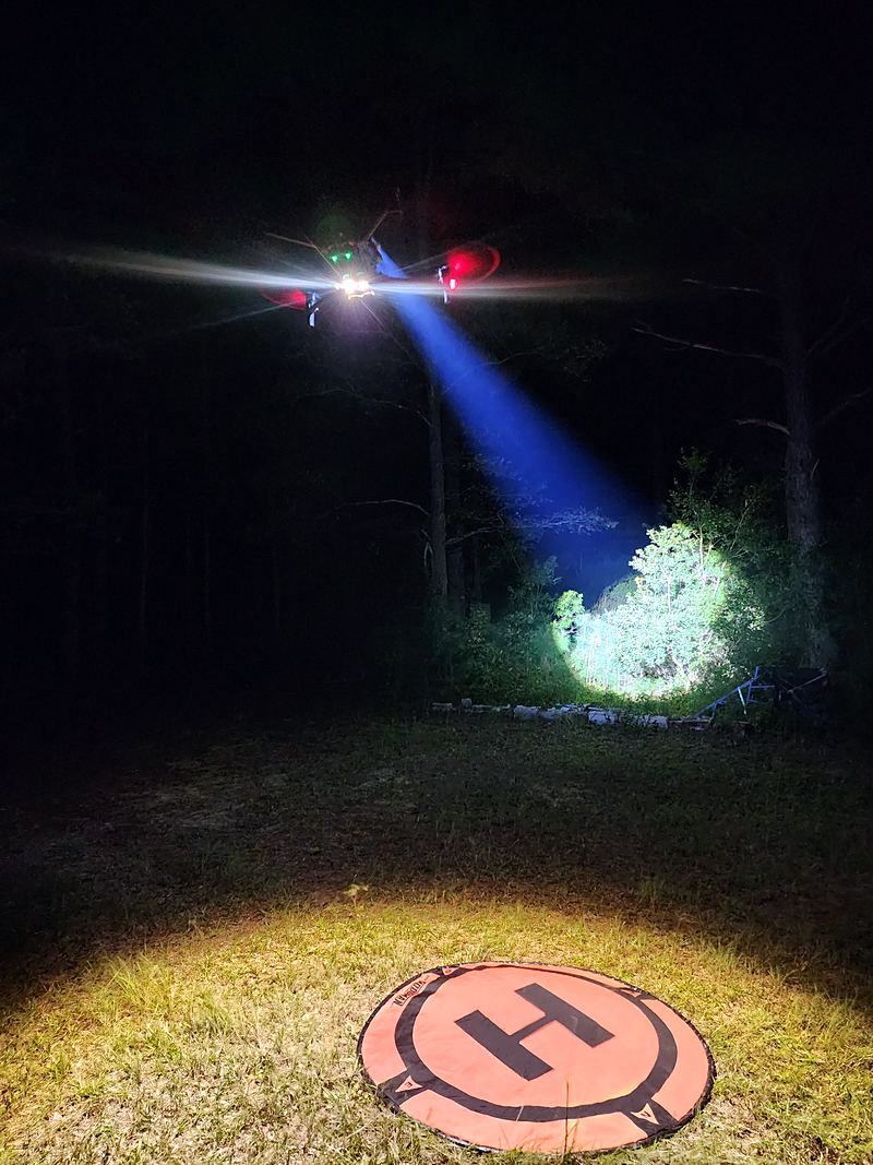 The thermal drone lifting off the landing pad under spotlight at night